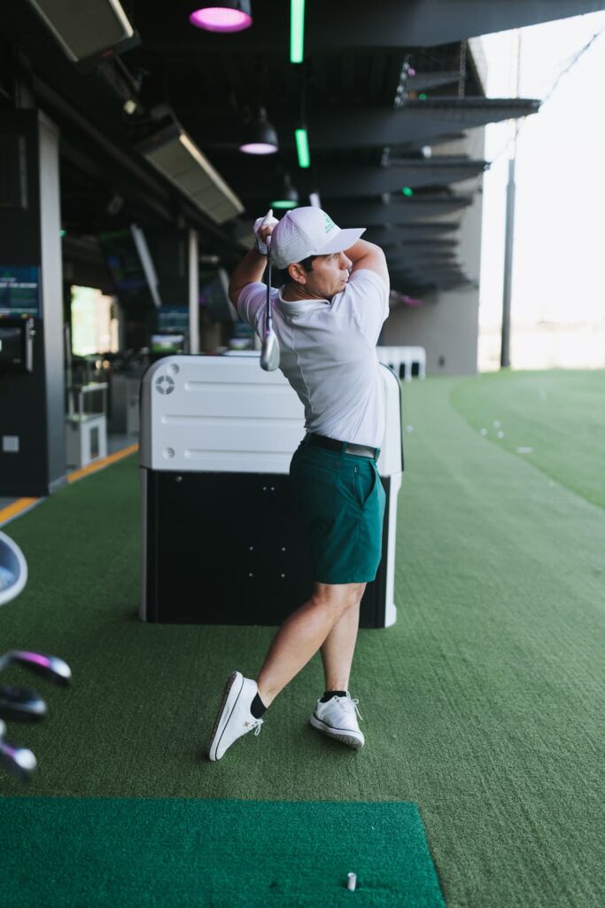 Man practicing his golf swing and form in a driving bay, used for golf lessons or performance improvement tips.